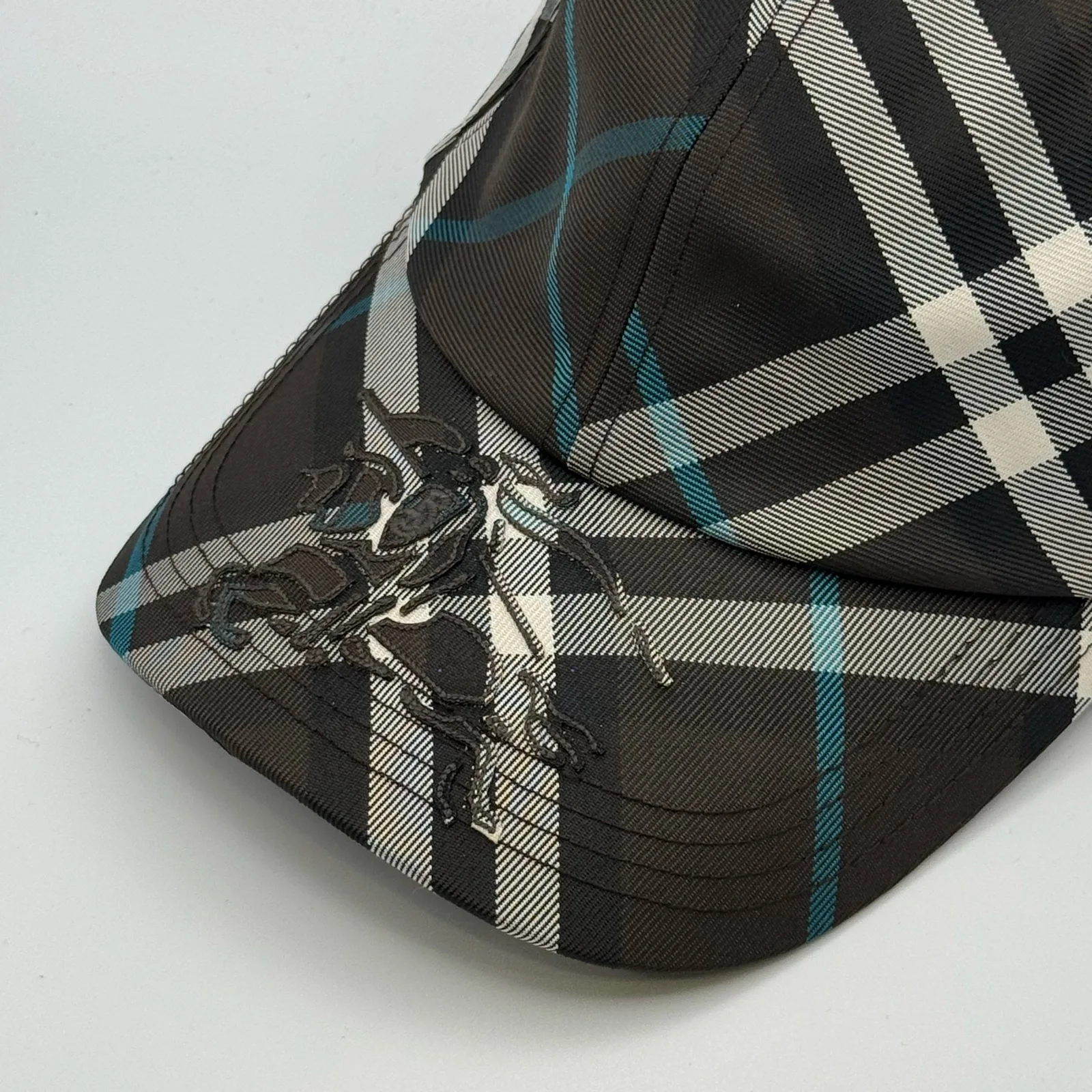 Close-up of the equestrian knight design embroidered on the brim of the dark brown check cap.