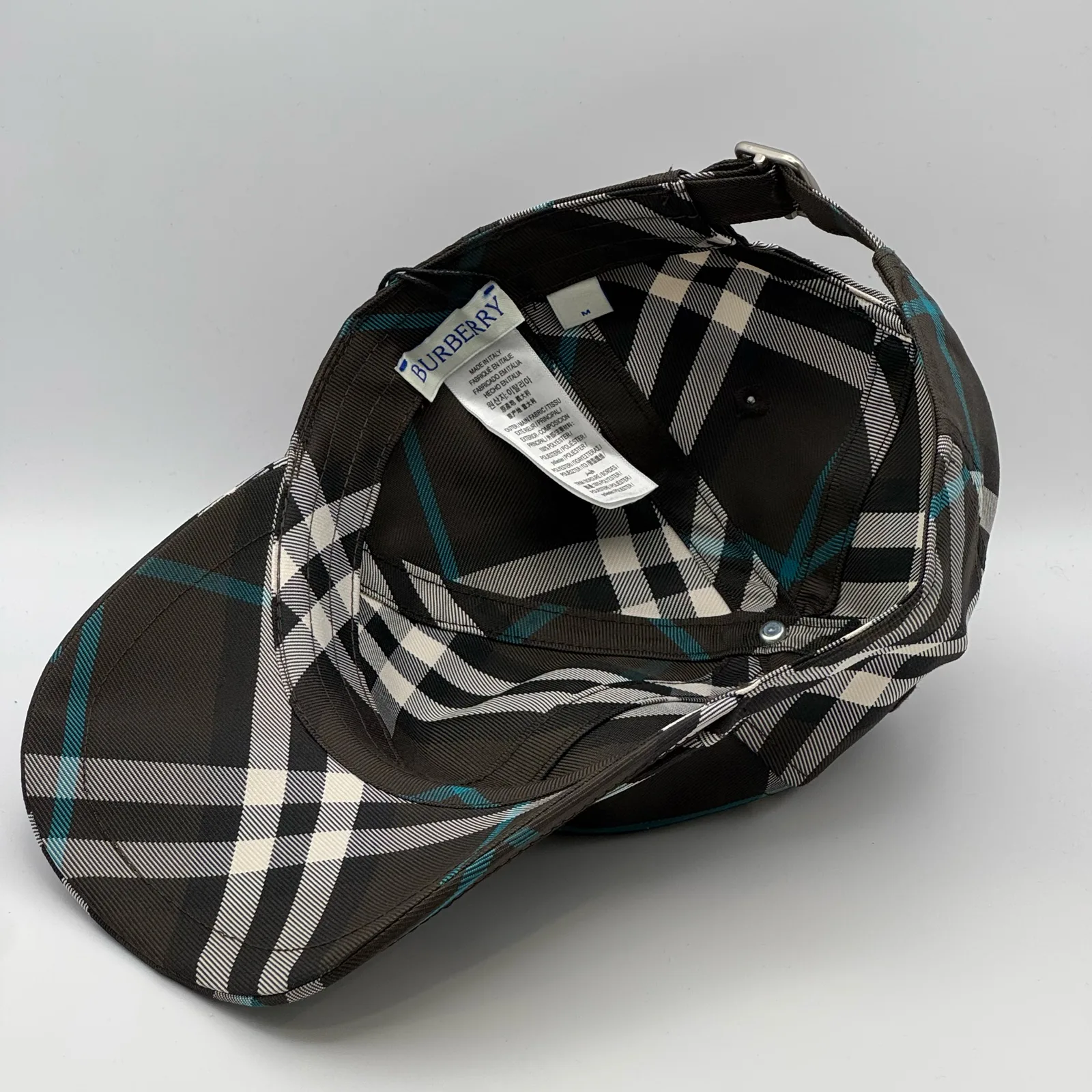 Underside of the dark brown check cap, brim lifted to show the interior and tag.