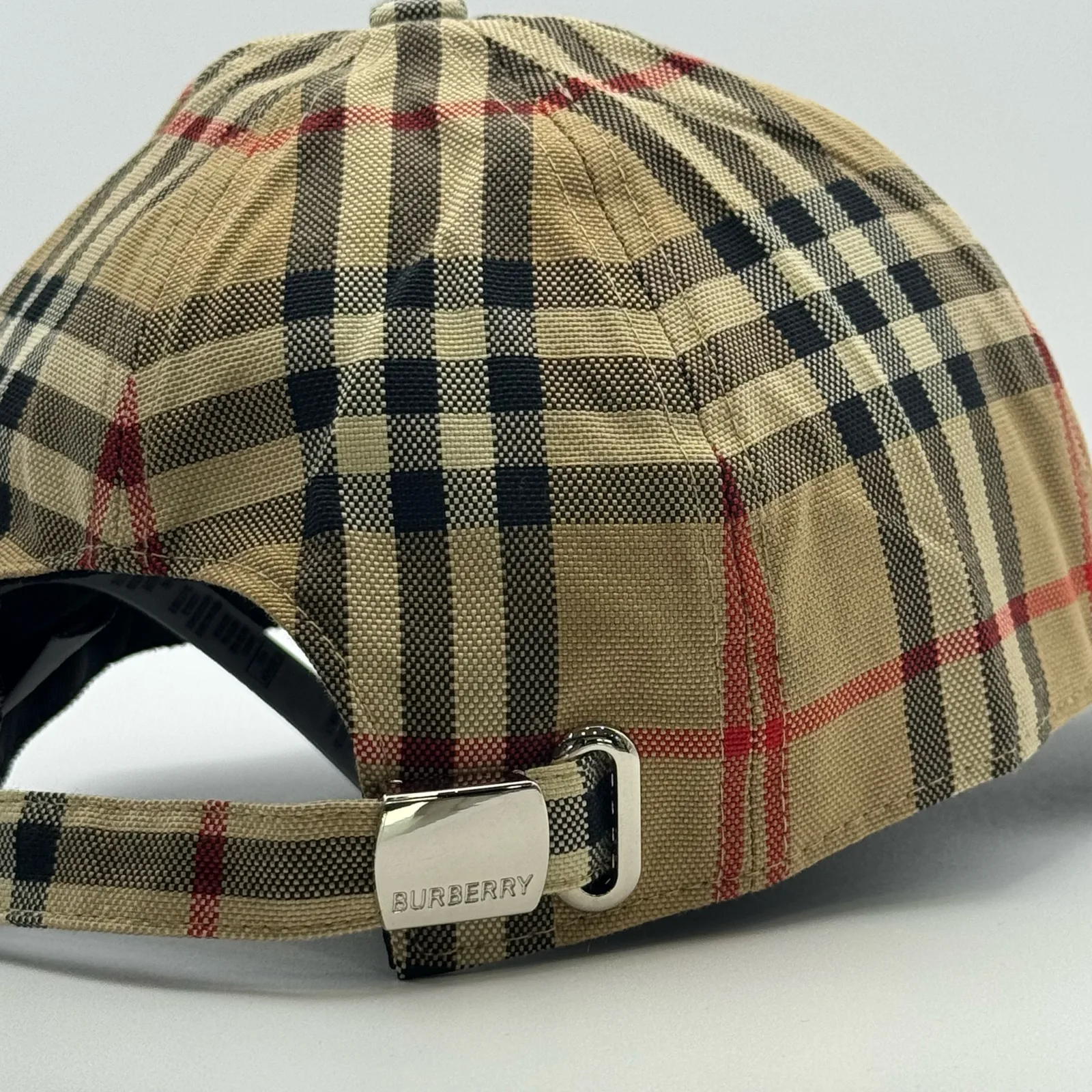 Close-up of the buckle strap at the back of the archive beige check cap.