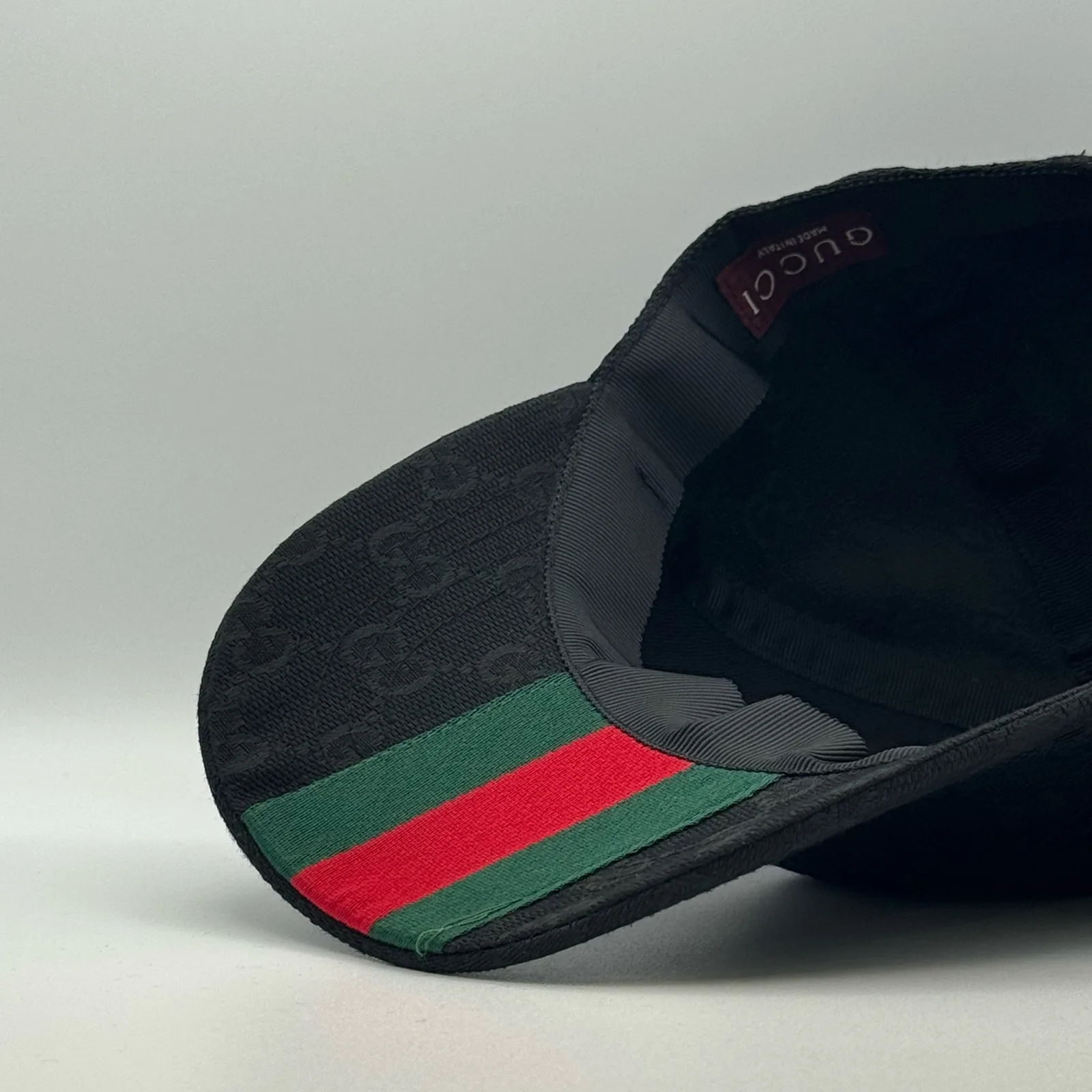 Black GG canvas cap, side view with brim lifted showing the web stripe lining