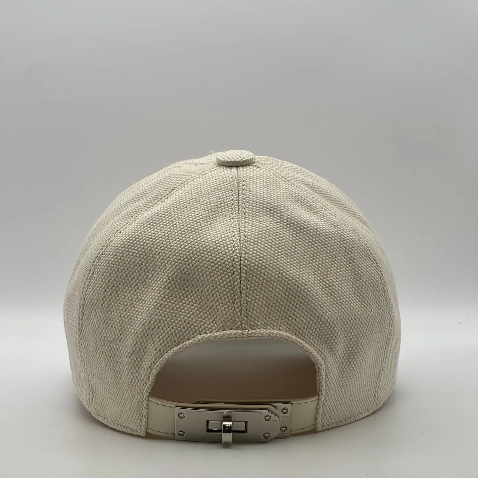 Hermès canvas cap, back view showing the cream leather strap and metal buckle closure.