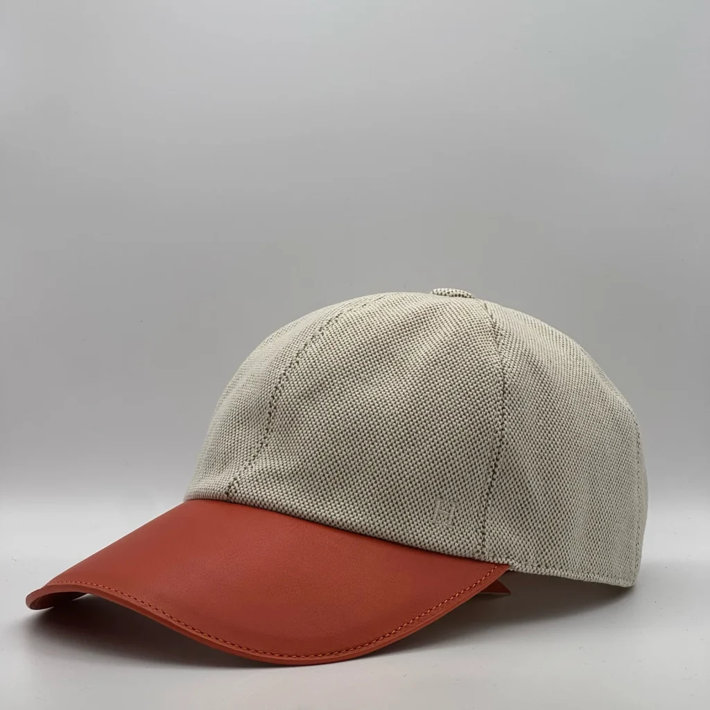 Hermès canvas cap, three-quarter view showing the rust-orange leather brim and tonal button.