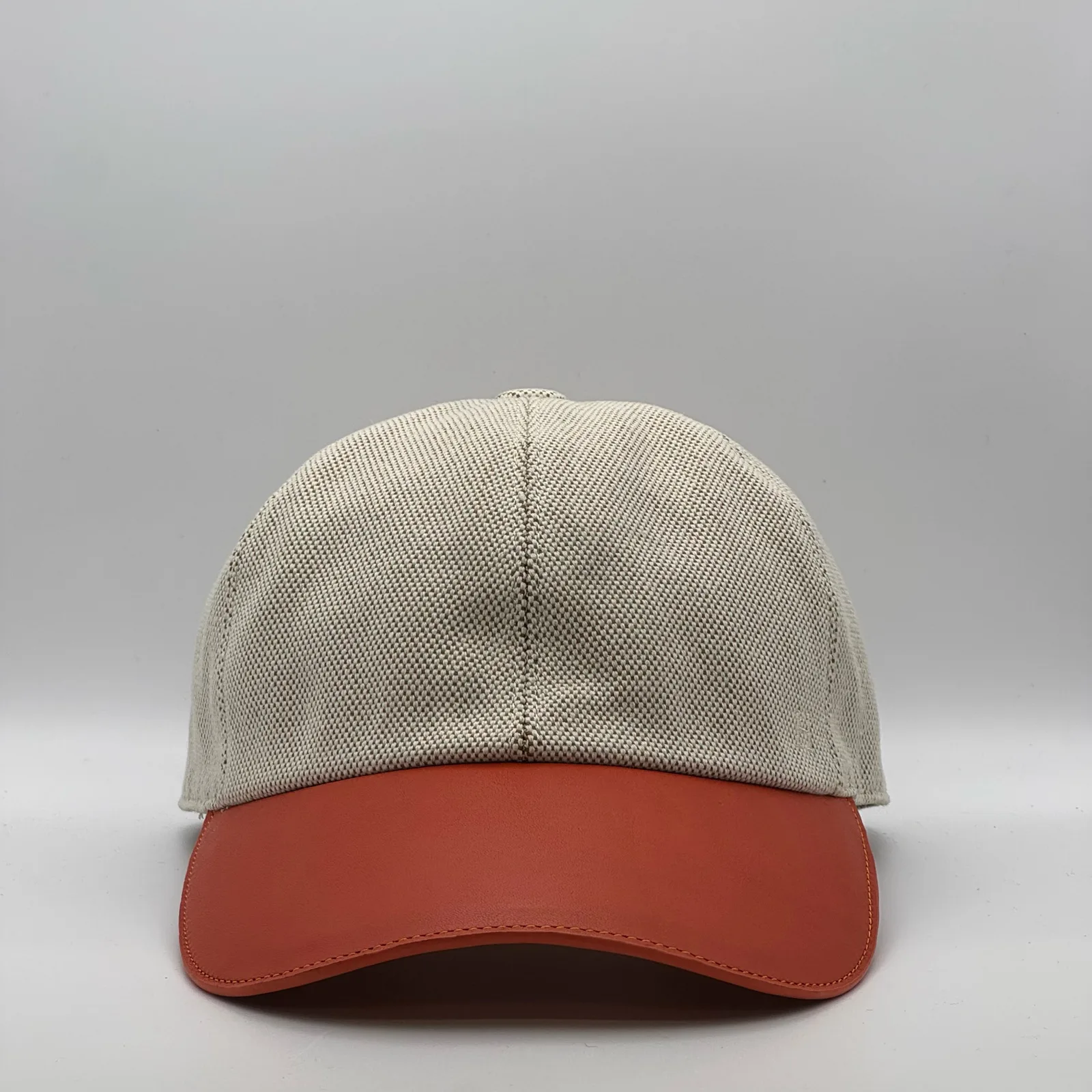 Hermès canvas cap, front view in oatmeal weave with a rust-orange leather brim.