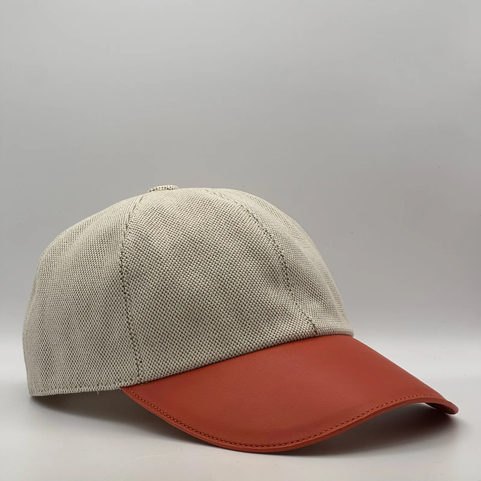 Hermès canvas cap, side profile in woven canvas with a rust-orange leather brim.