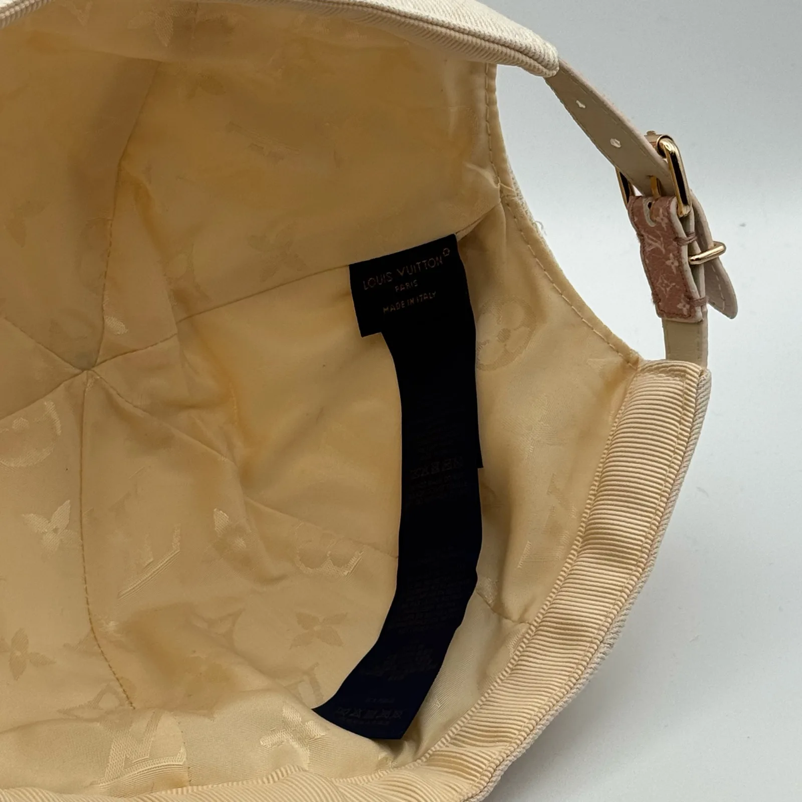 Inside view of the beige cap showing the lining and leather strap.